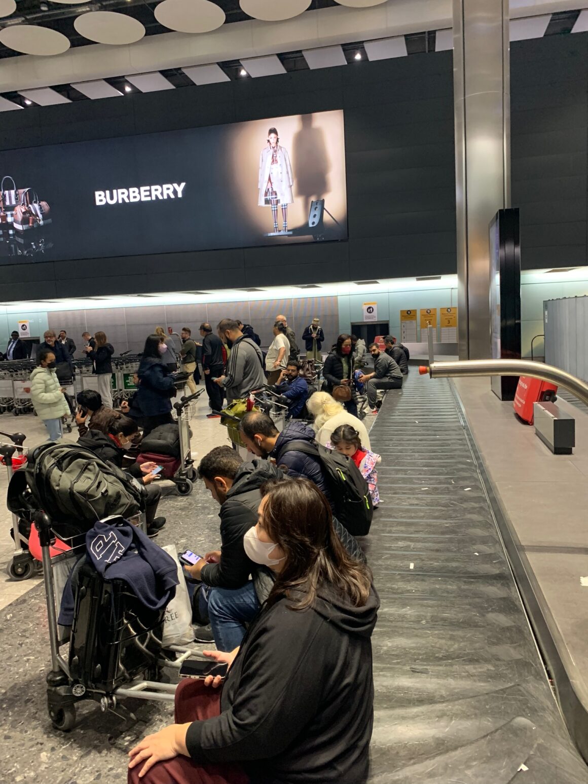 Passengers sit on edge of baggage belts waiting at Heathrow 19 December 2022