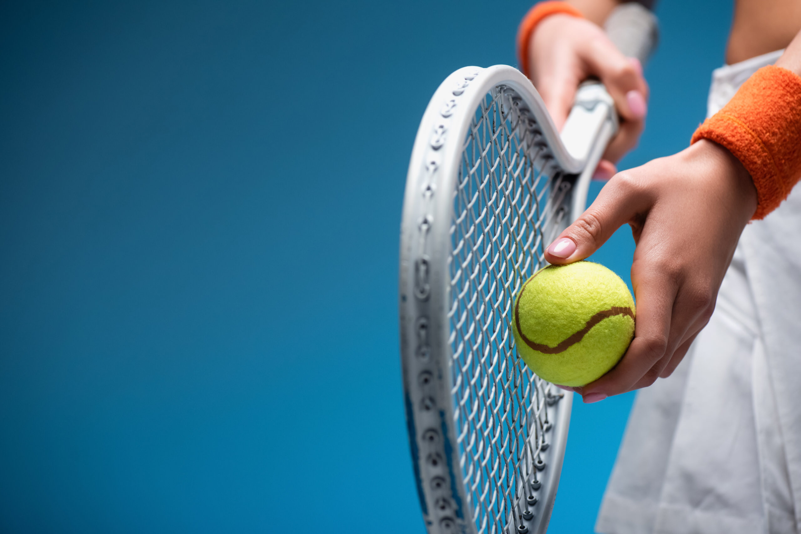 运动型年轻女子在蓝色打球时拿着网球拍和球的部分视图