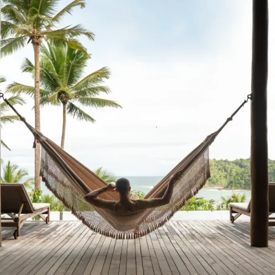 A photo of a Man Sitting on a swing with some coconut trees and a great view