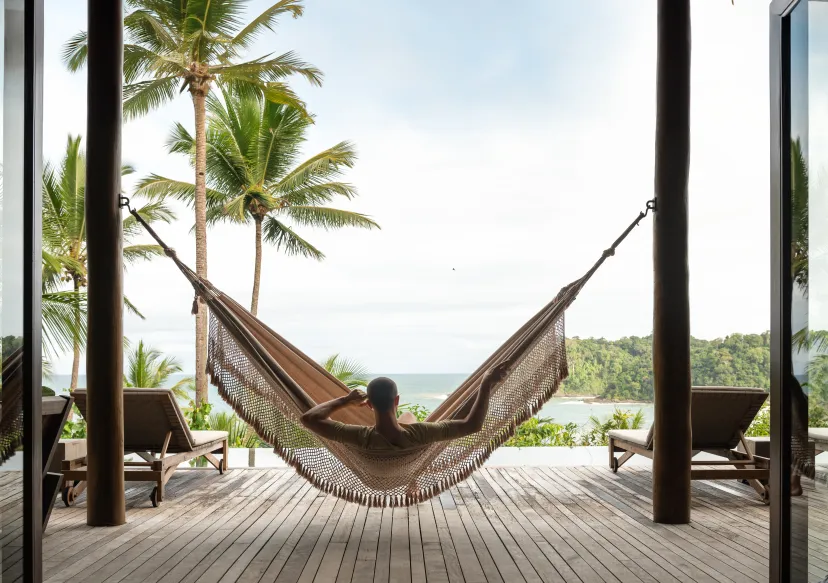 A photo of a Man Sitting on a swing with some coconut trees and a great view